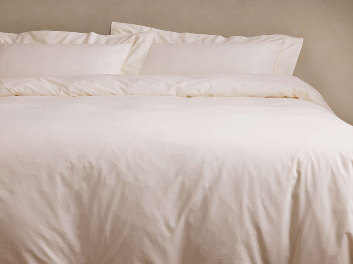 Soft, off-white Washed Percale Duvet, gently wrinkled, on a bed with two matching pillow shams, against a plain wall.