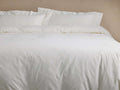 Washed Sateen Duvet in off-white, neatly but softly draped on a bed with two matching pillows, showcasing its relaxed texture.
