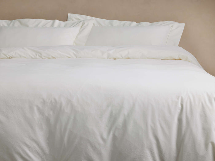 Washed Sateen Duvet in off-white, neatly but softly draped on a bed with two matching pillows, showcasing its relaxed texture.
