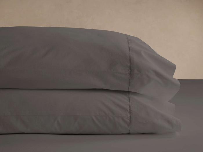Two dark gray Washed Sateen Pillowcases stacked neatly, showcasing their subtle sheen and decorative stitching.