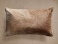 Tan hide lumbar pillow with varied brown and tan fur texture, rectangular shape, and white whipstitching along its edges.