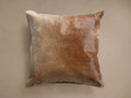 Square brown hide pillow with varied shades, featuring white whipstitch edges, shown slightly angled on a light brown background.