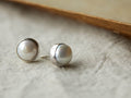 Silver stud earrings featuring round freshwater pearls on a textured surface with post backs visible.