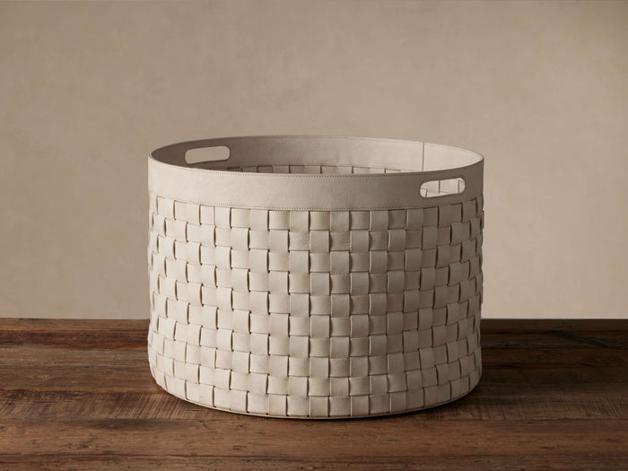 Light-colored Wilona Nubuck Basket, woven, cylindrical with reinforced handles, sits on a wooden floor against a plain wall.