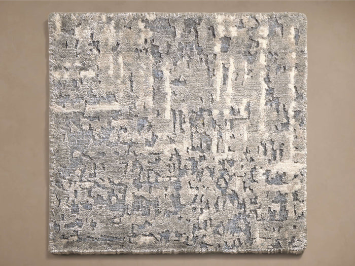 Top-down view of a rectangular rug featuring an abstract textured pattern in light grey, dark grey, and muted blue tones.