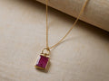 Yaelle Necklace: Gold-plated chain with a rectangular deep pink silimanite pendant, angled on textured cream fabric with a roll behind.