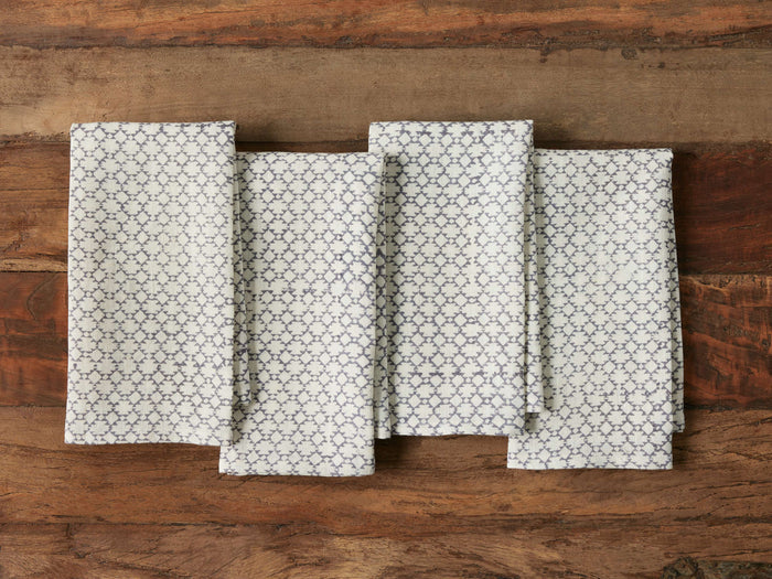 Zadie Napkins set of 4 displayed on a wooden surface. Each napkin has a geometric block-printed pattern in blue on white linen fabric.