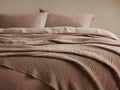 Zehra Clay Linen Bed Blanket draped over a bed, revealing its soft, gauzy, crinkled texture. Clay-colored pillows behind.